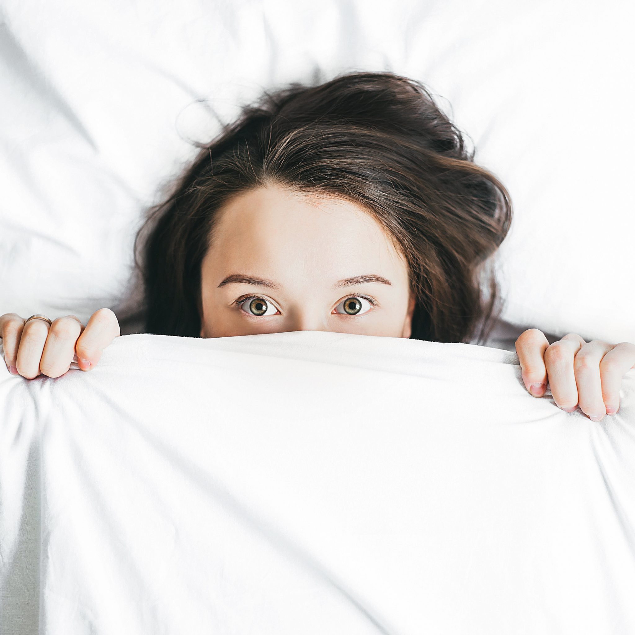 Woman laying in bed with covers over her face (living on a budget)